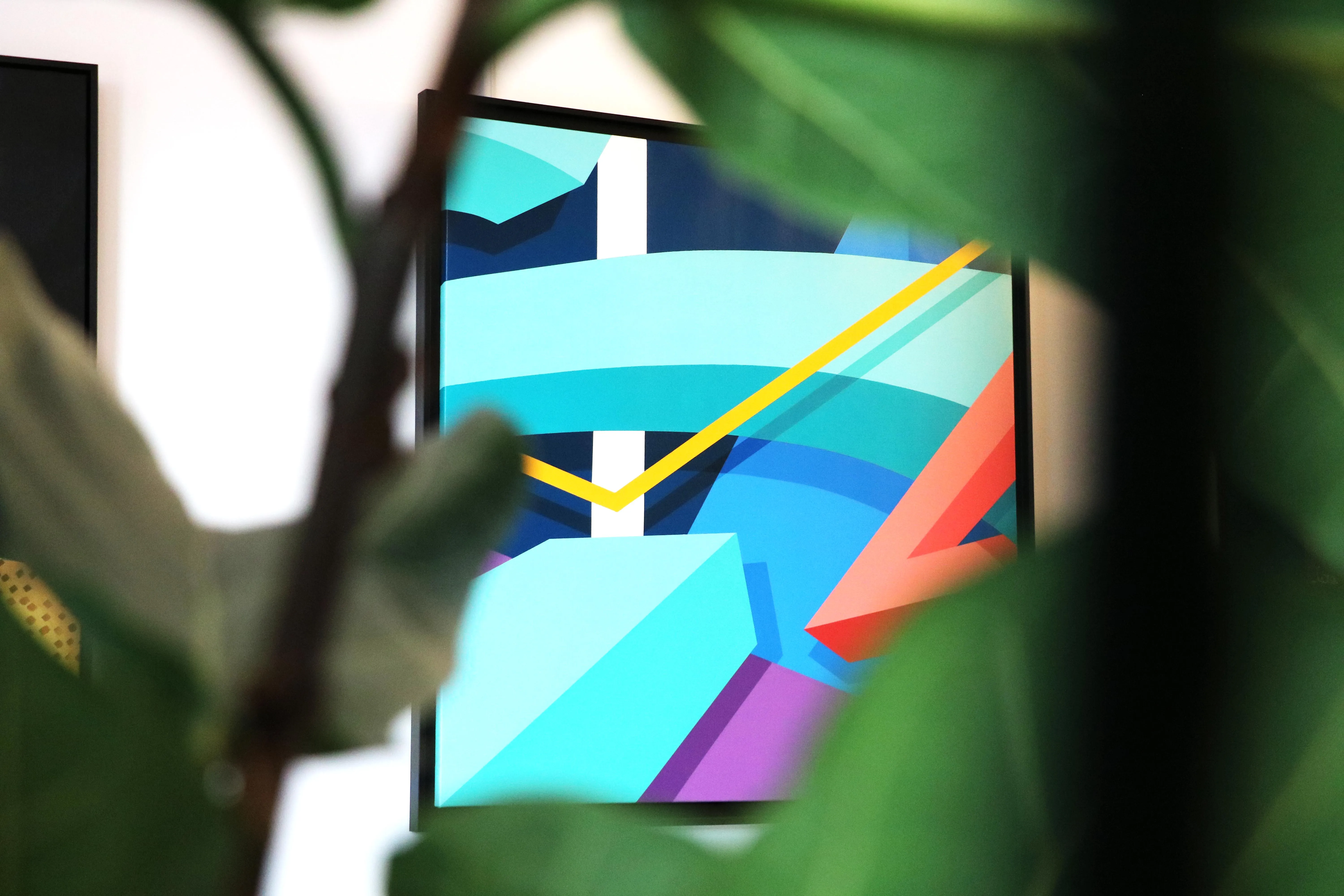 Œuvre abstraite et géométrique aux couleurs vives vue à travers des feuilles