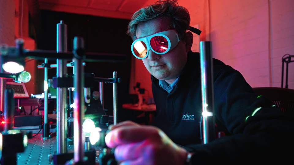 A HoloMem engineer in laser safety goggles adjusting optics in the lab