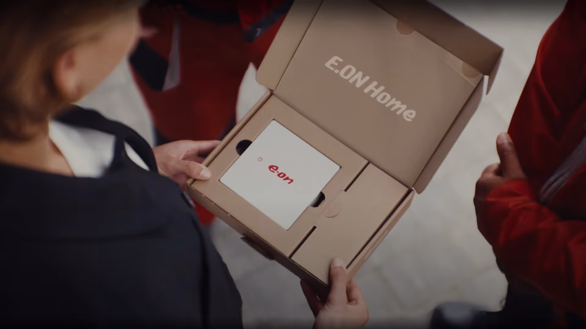 Person hält geöffnete E.ON Home Verpackung mit weißem Gerät und rotem E.ON-Logo.