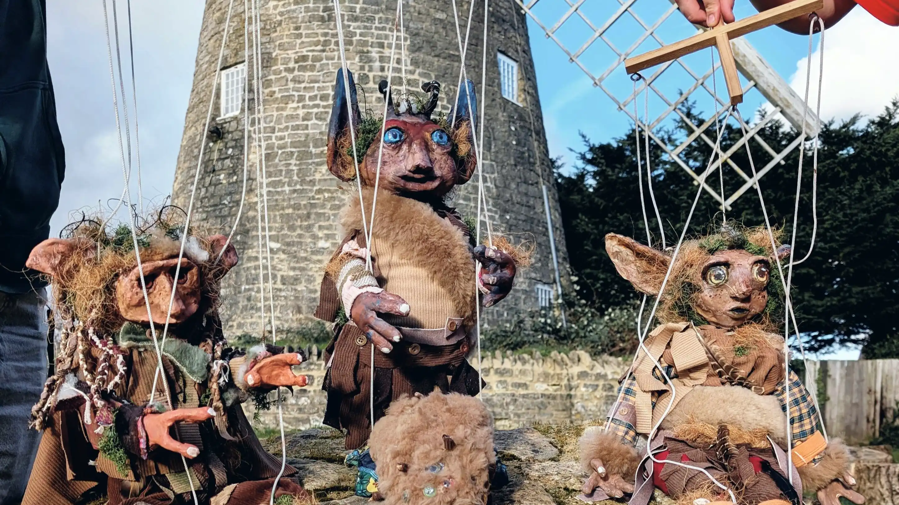 Three detailed faerie marionette puppets posed outdoors with a stone building and trees behind.