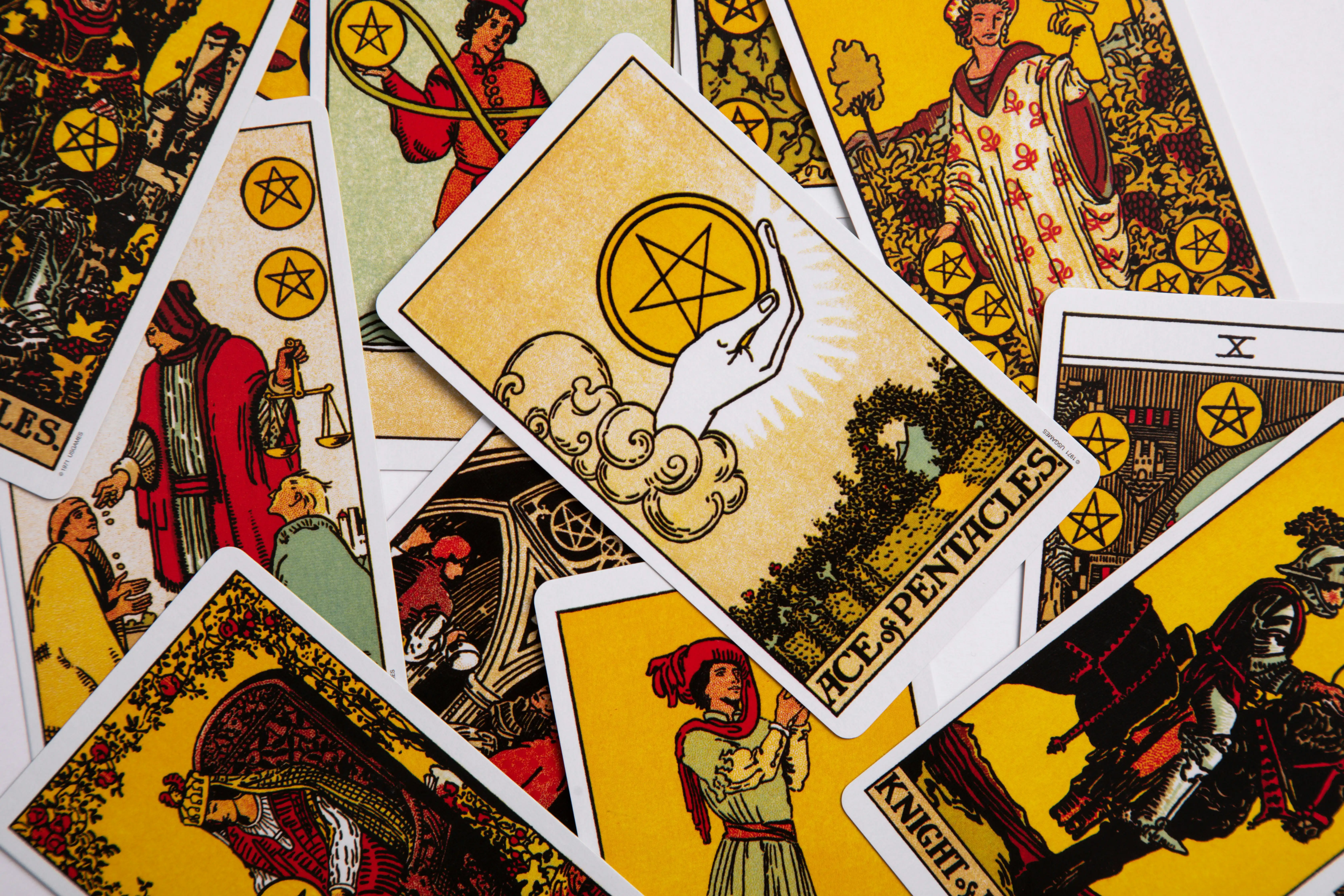 A pile of colorful tarot cards featuring various suits and the Ace of Pentacles card on top.