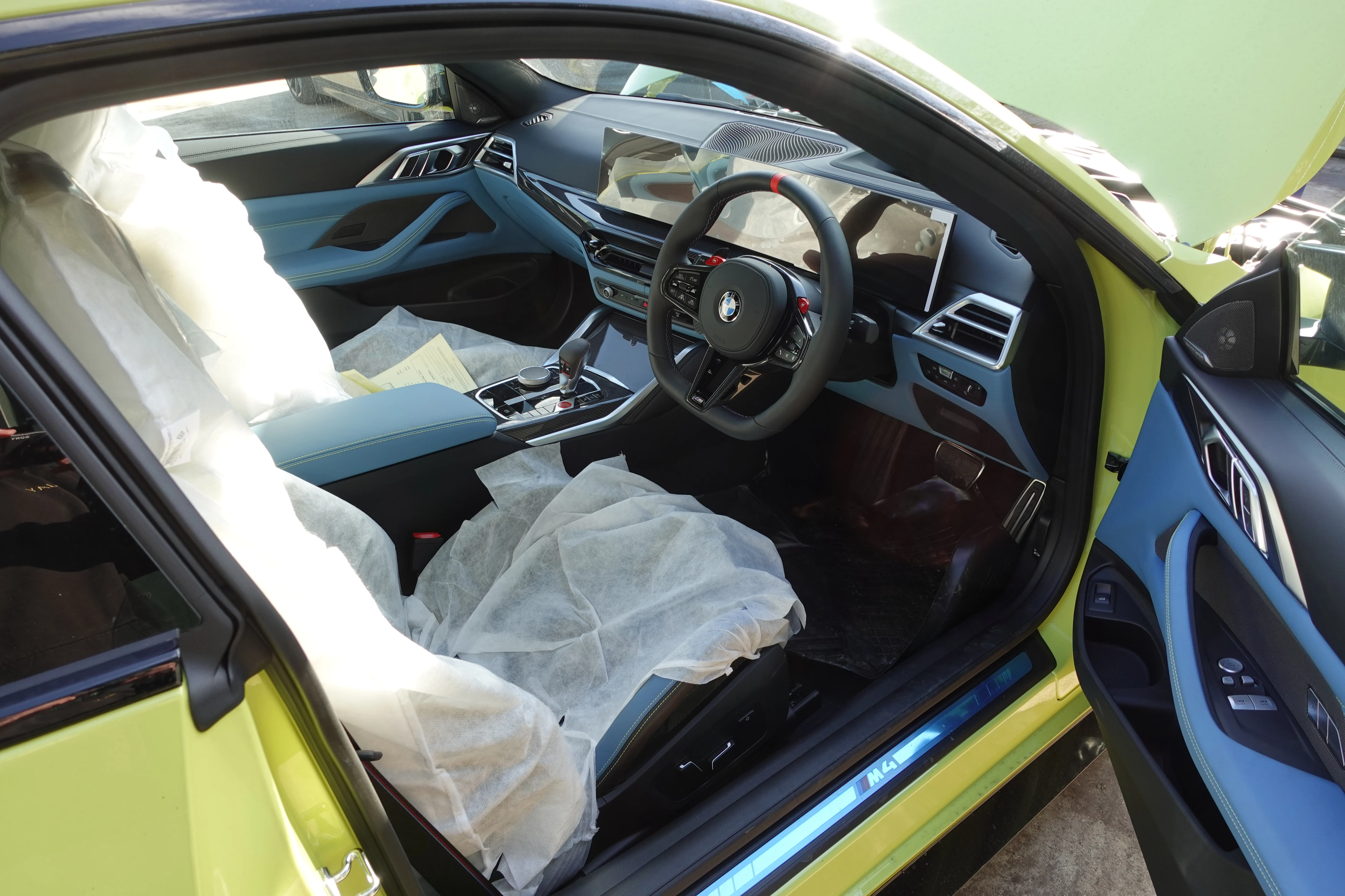 A brand new BMW M4 arriving on a trailer directly from BMW, with all protective wrapping on the interior and exterior still present.