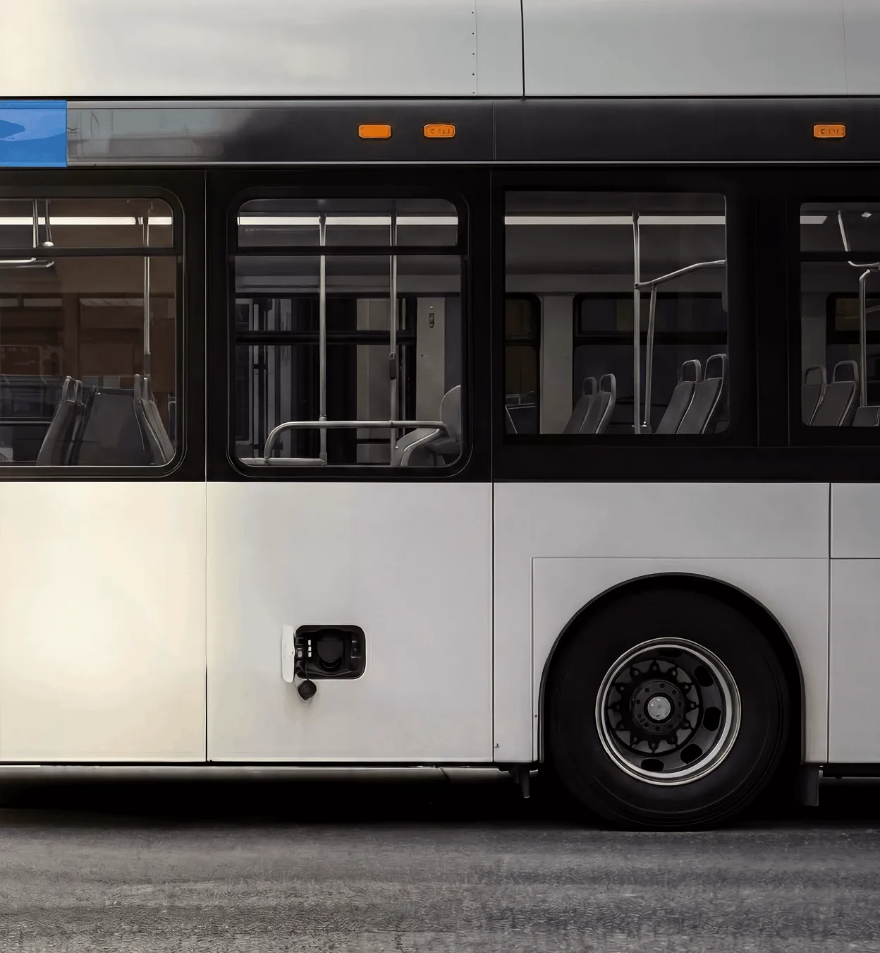 Side view of a white and black city bus with visible empty seats and a rear wheel.