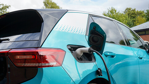Close-up of a turquoise electric car charging with a cable connected to its rear port.