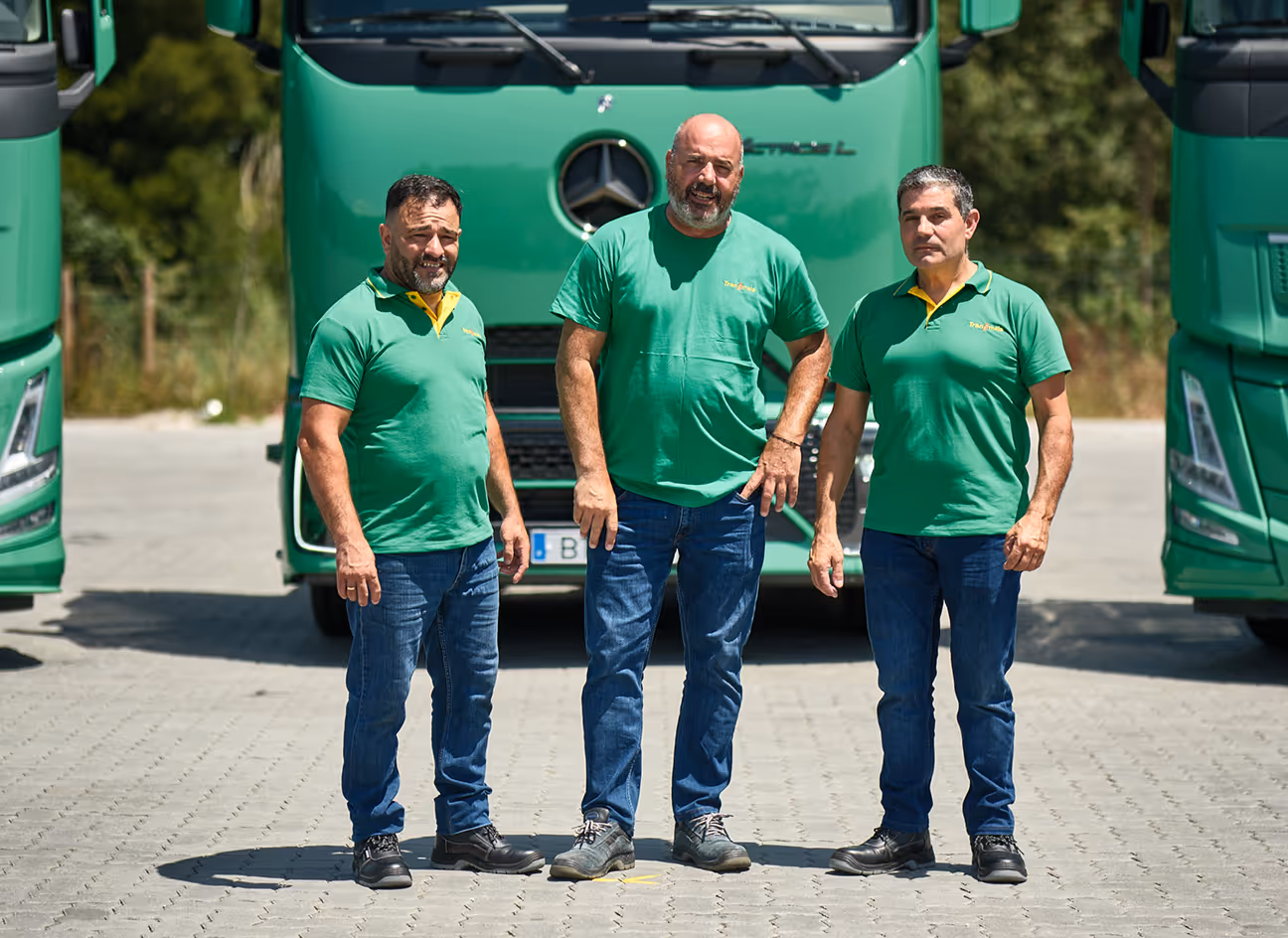 Três motoristas da Transmaia em frente à frota de camiões