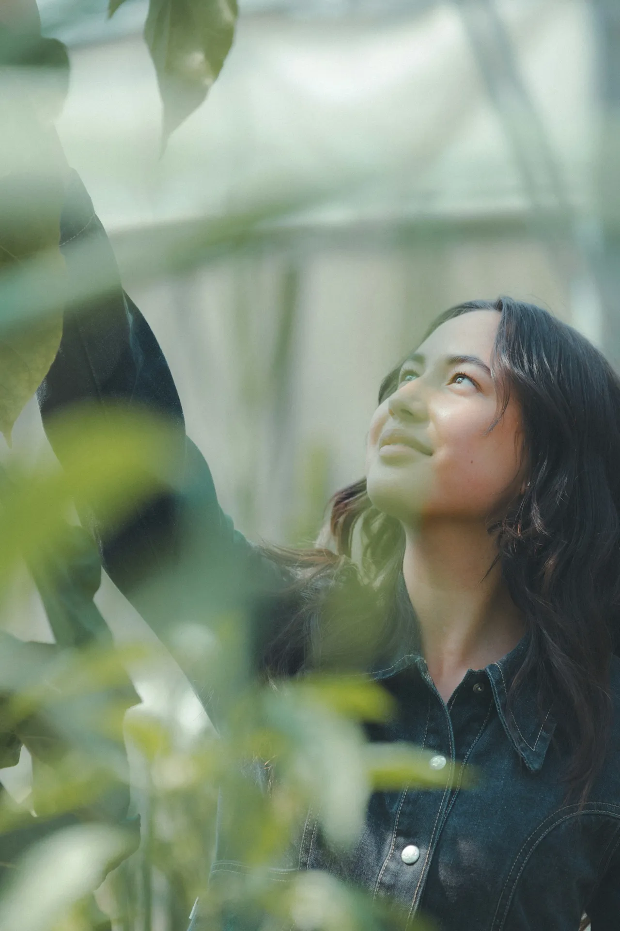 Woman smiling as she looks up among plants in a greenhouse
