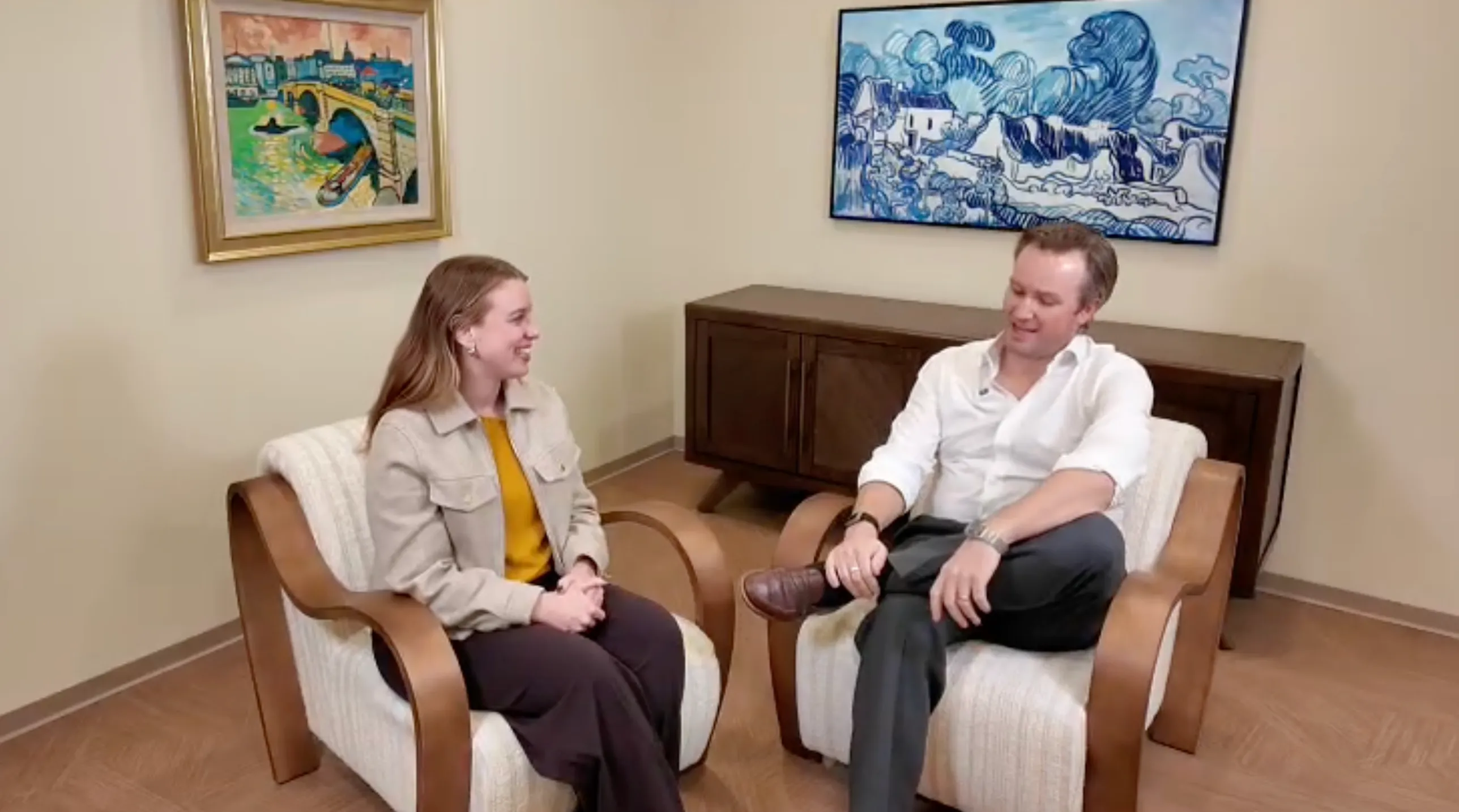 Mindy Green and Dr. Reynolds Lawnin seated in armchairs talking in the office lounge, video still