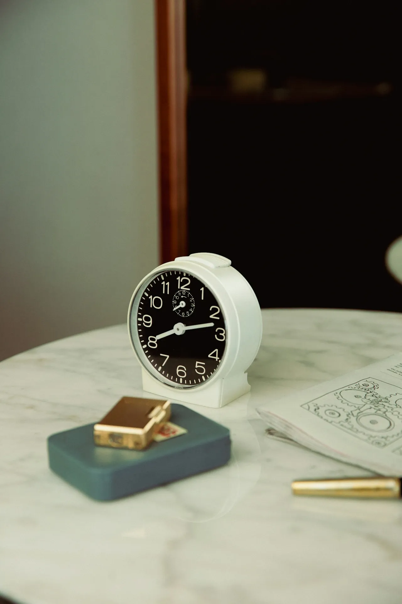 Black alarm clock and a pen on a marble table