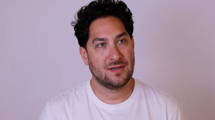 Patient with dark curly hair in a white T-shirt speaking in a video testimonial