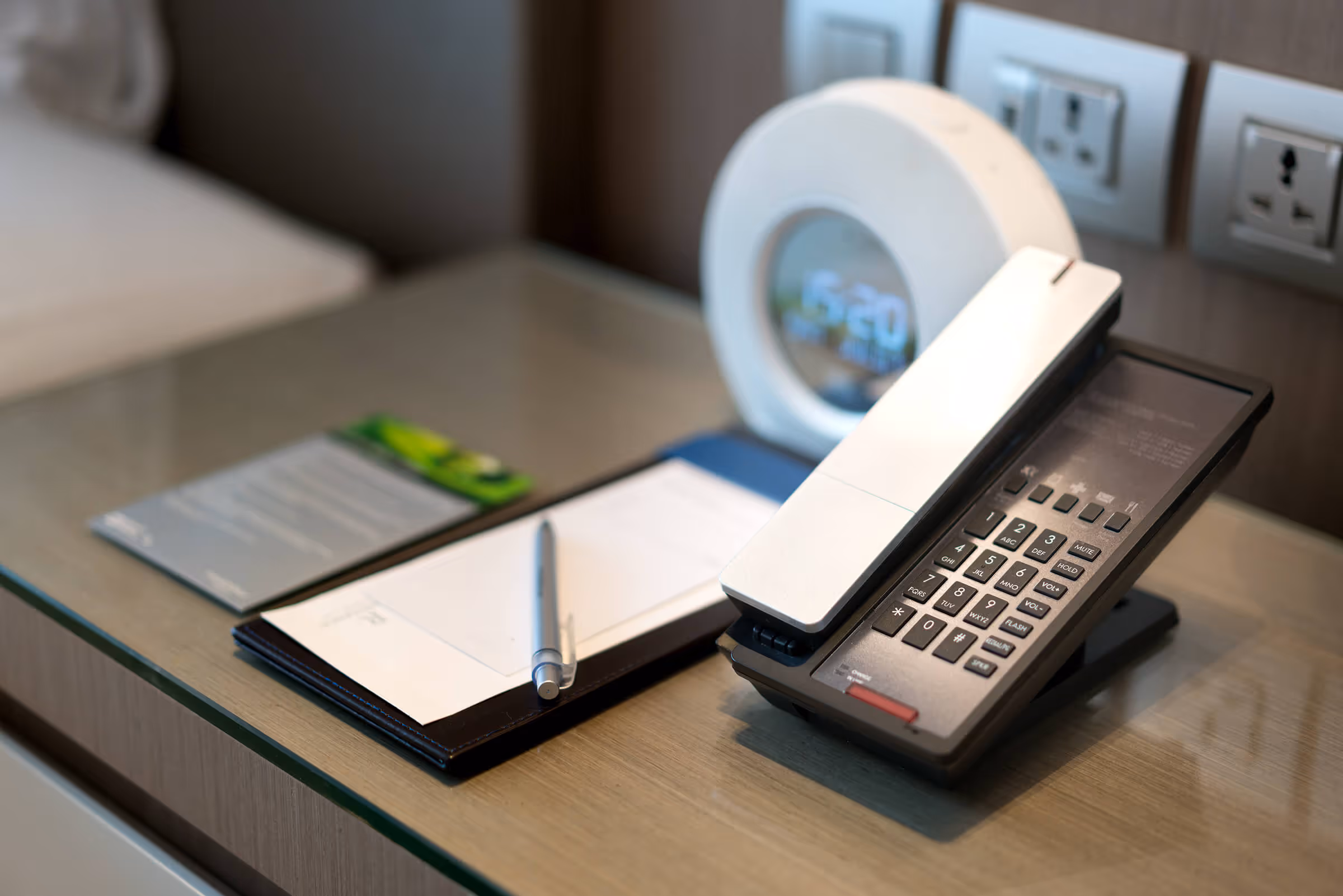 Hotel guest room desk with a modern hotel phone, notepad, and bedside clock.
