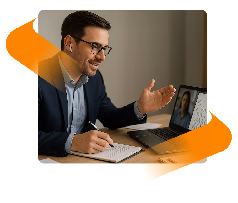 Man in glasses and suit wearing earbuds, smiling and gesturing during a video call while taking notes.