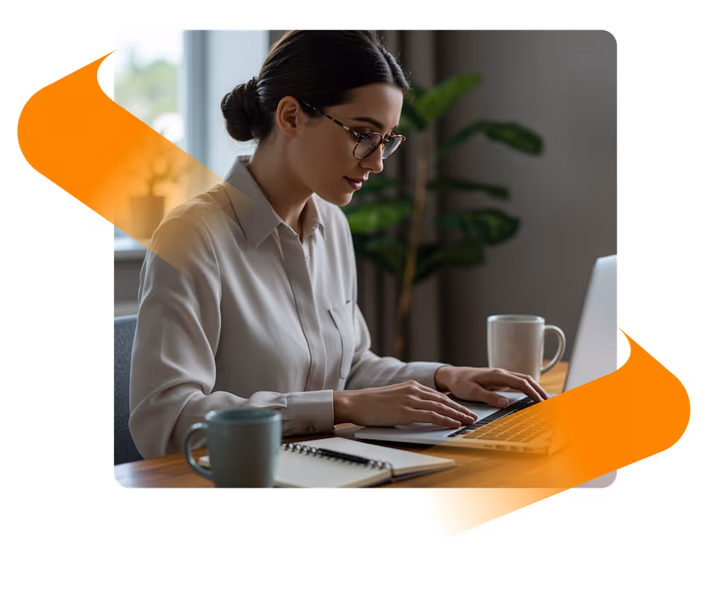 Woman wearing glasses and a beige blouse typing on a laptop at a wooden desk with coffee mugs and a notebook nearby.