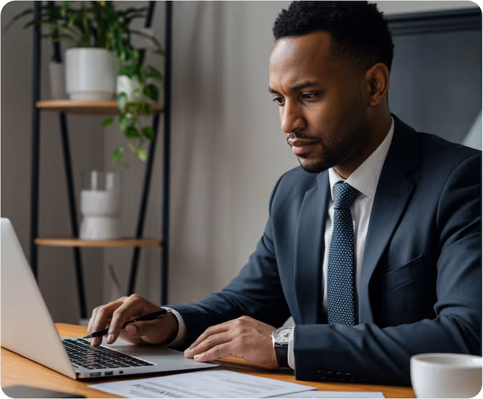 Professional man in a suit working on a laptop at a desk with documents and a coffee cup.