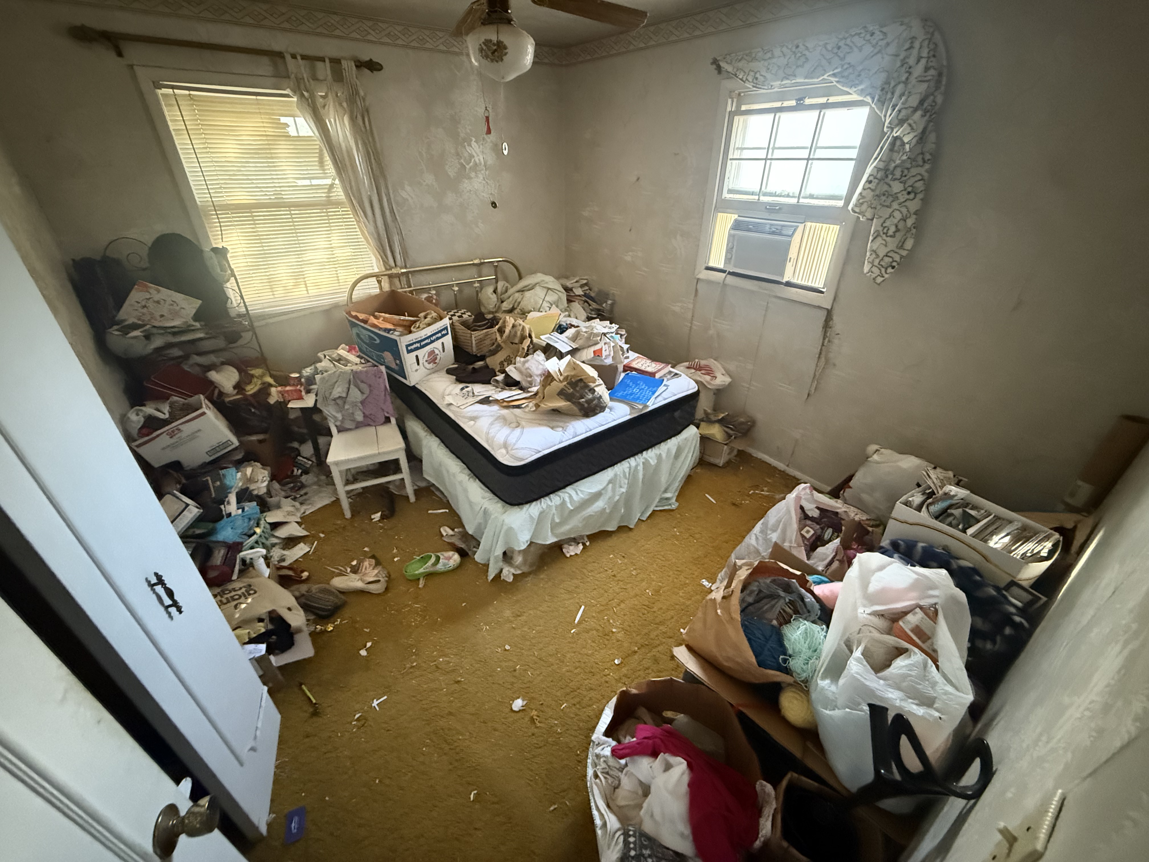 Junk inside of a home in Fairlawn Ohio that is full of trash, clothes, and a bed in the corner.