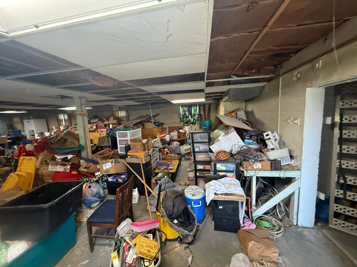 A direct shot of a garage full of clutter , wood , furniture , doors, ect. it looks unorganized.