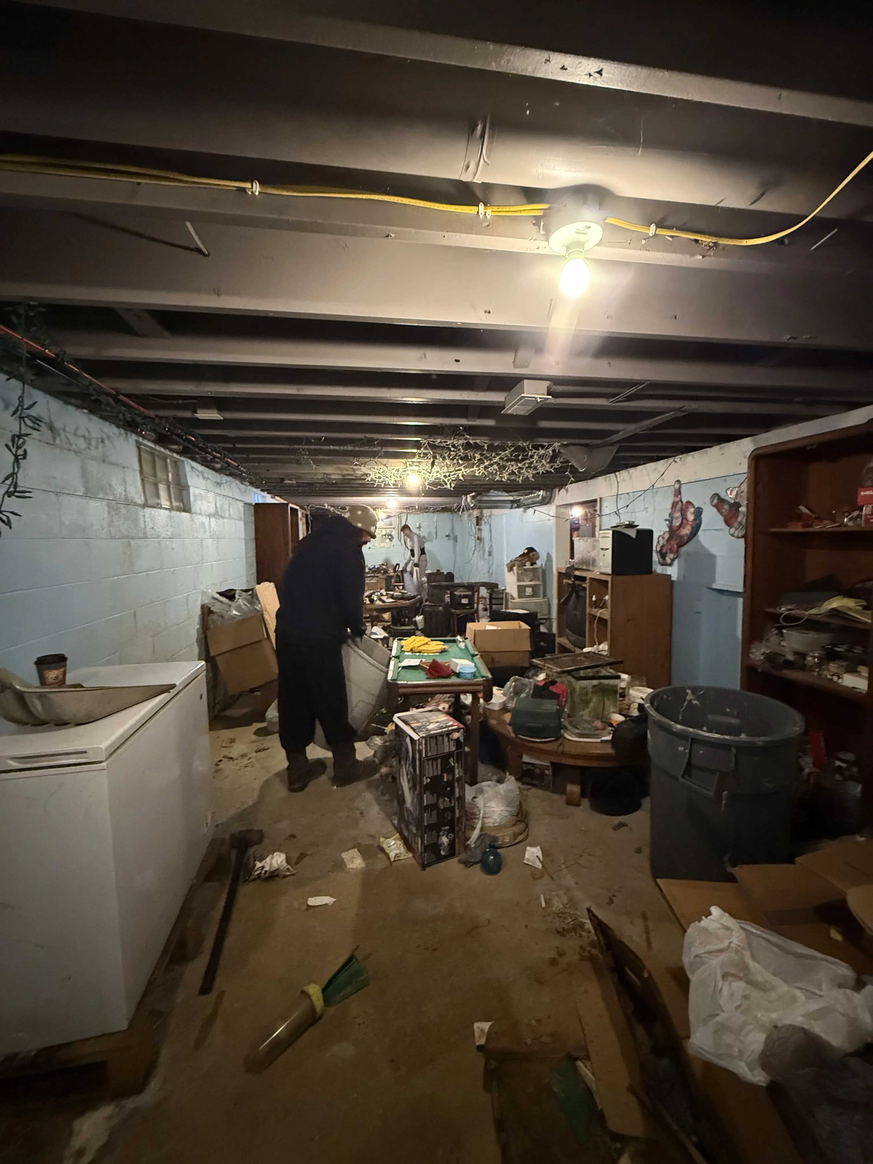 A direct shot of a garage full of clutter , wood , furniture , doors, ect. it looks unorganized.