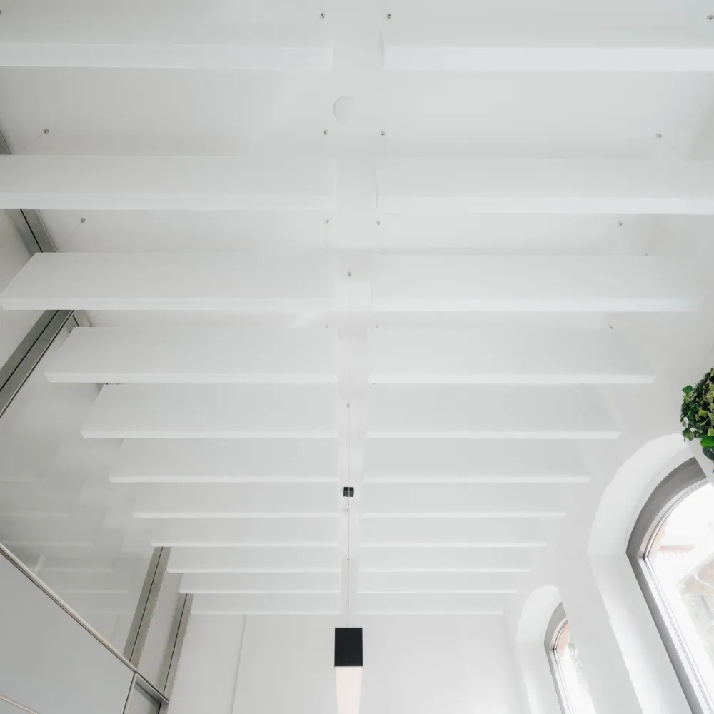 Weiße Akustik-Baffeln an der Decke eines Raums mit Rundbogenfenster