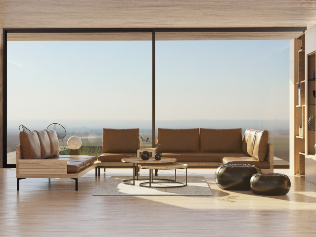 Salon moderne avec grands canapés en cuir marron, tables basses rondes en bois et métal, deux poufs noirs, tapis clair, grandes fenêtres offrant une vue dégagée sur le paysage extérieur.