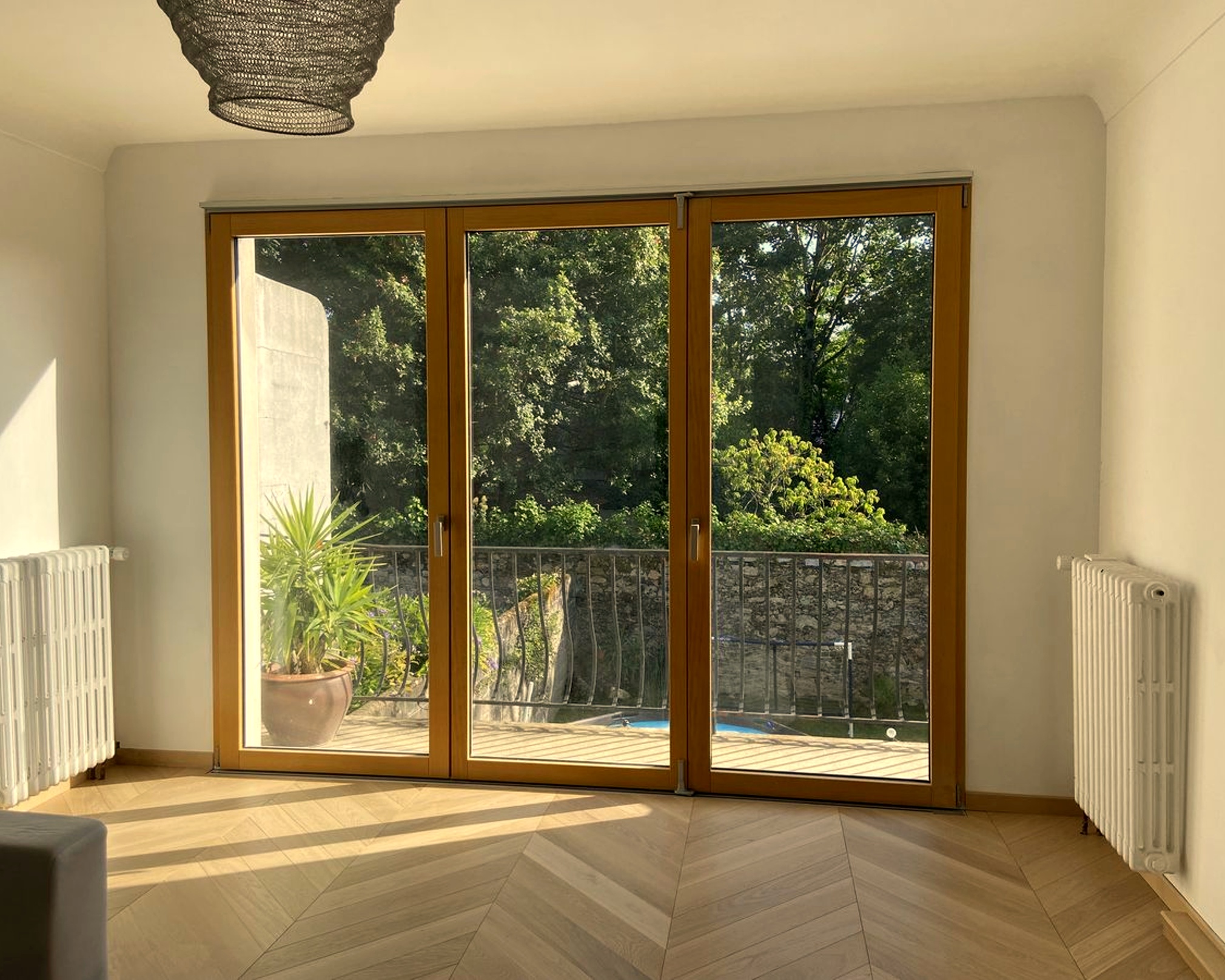 Grandes portes vitrées donnant sur un balcon avec vue sur un jardin verdoyant et un pot de plante.