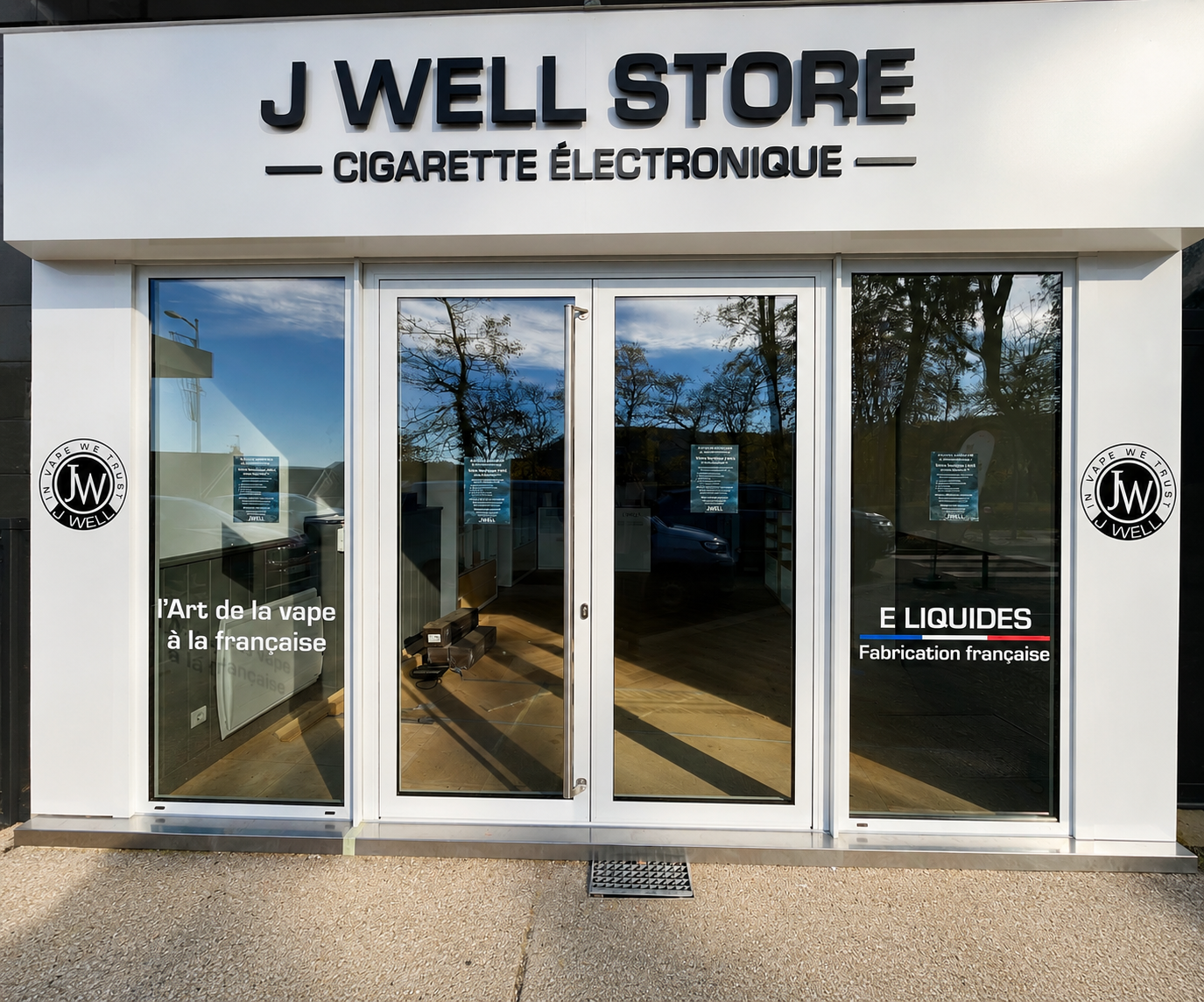 Façade d'un magasin nommé J WELL STORE avec enseigne signalant vente de cigarettes électroniques, vitres avec textes en français sur vape et e-liquides de fabrication française.