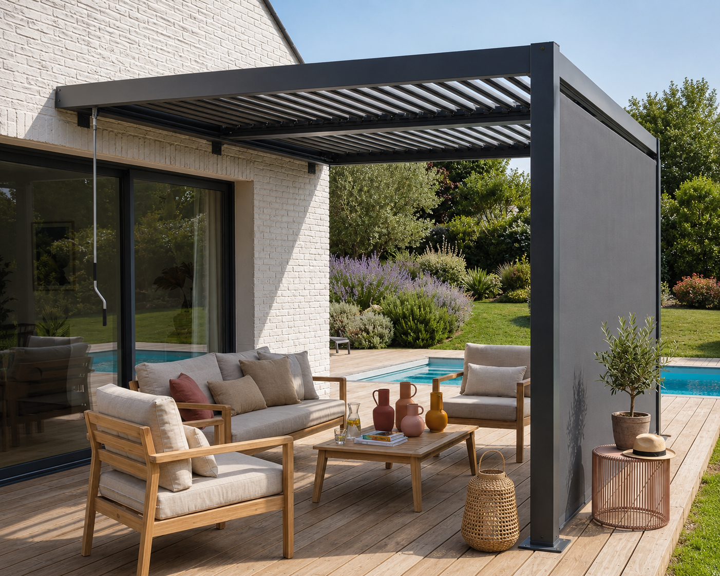 Terrasse en bois avec sofa, fauteuils en bois et coussins beiges sous une pergola moderne en métal gris, vue sur piscine et jardin fleuri en arrière-plan.