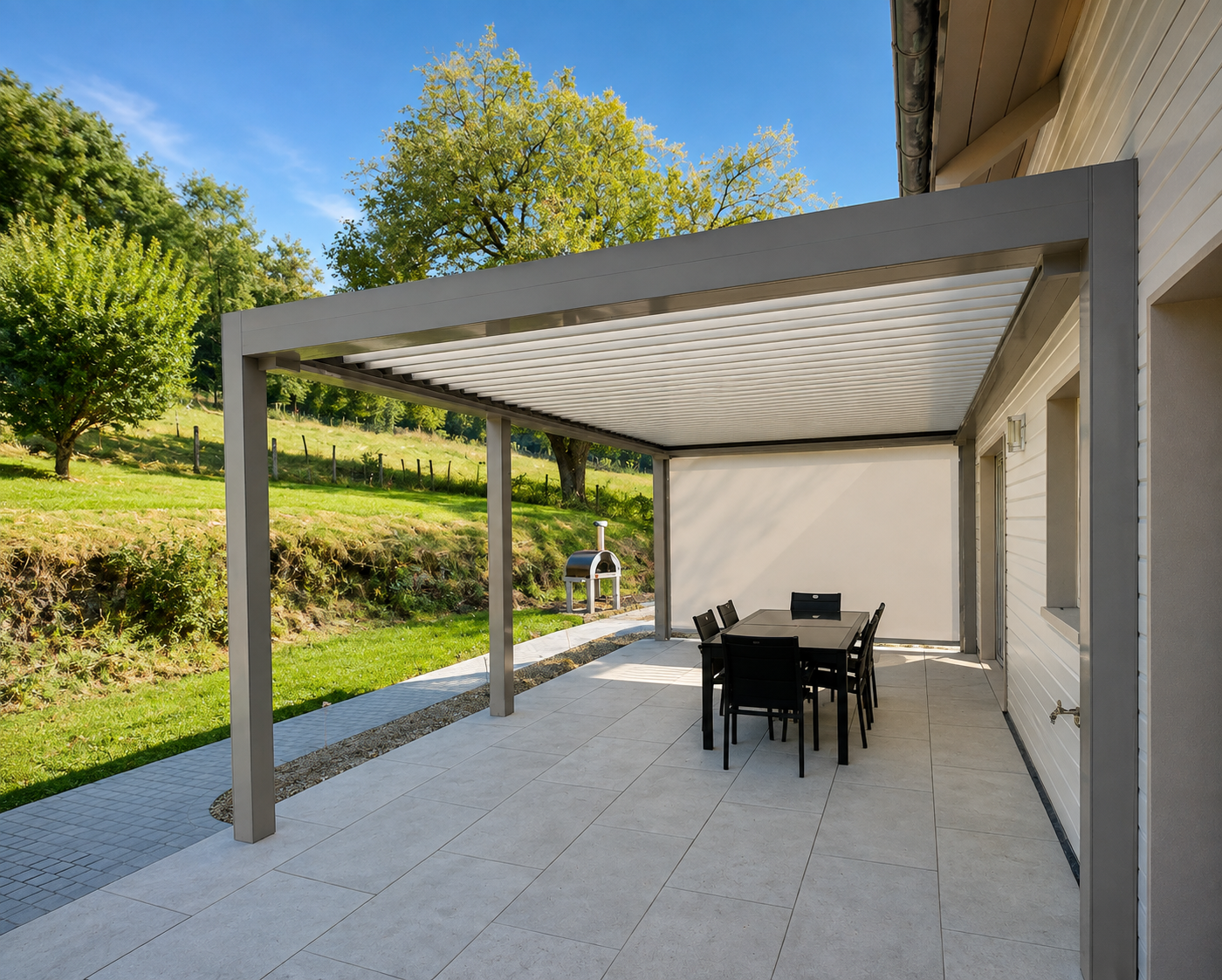 Terrasse moderne avec auvent en métal gris, table à manger noire de six chaises, barbecue à bois à l'extérieur, entourée d'un paysage de pelouse verte, arbres et ciel bleu clair.