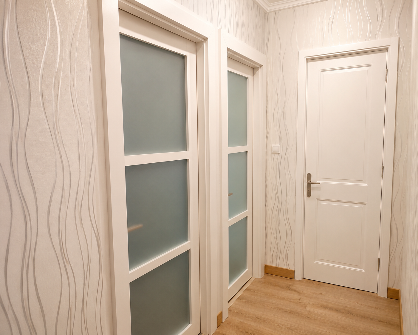 Couloir intérieur avec trois portes blanches : deux avec panneaux de verre dépoli et une porte pleine, murs avec papier peint à motifs ondulés, sol en bois clair.