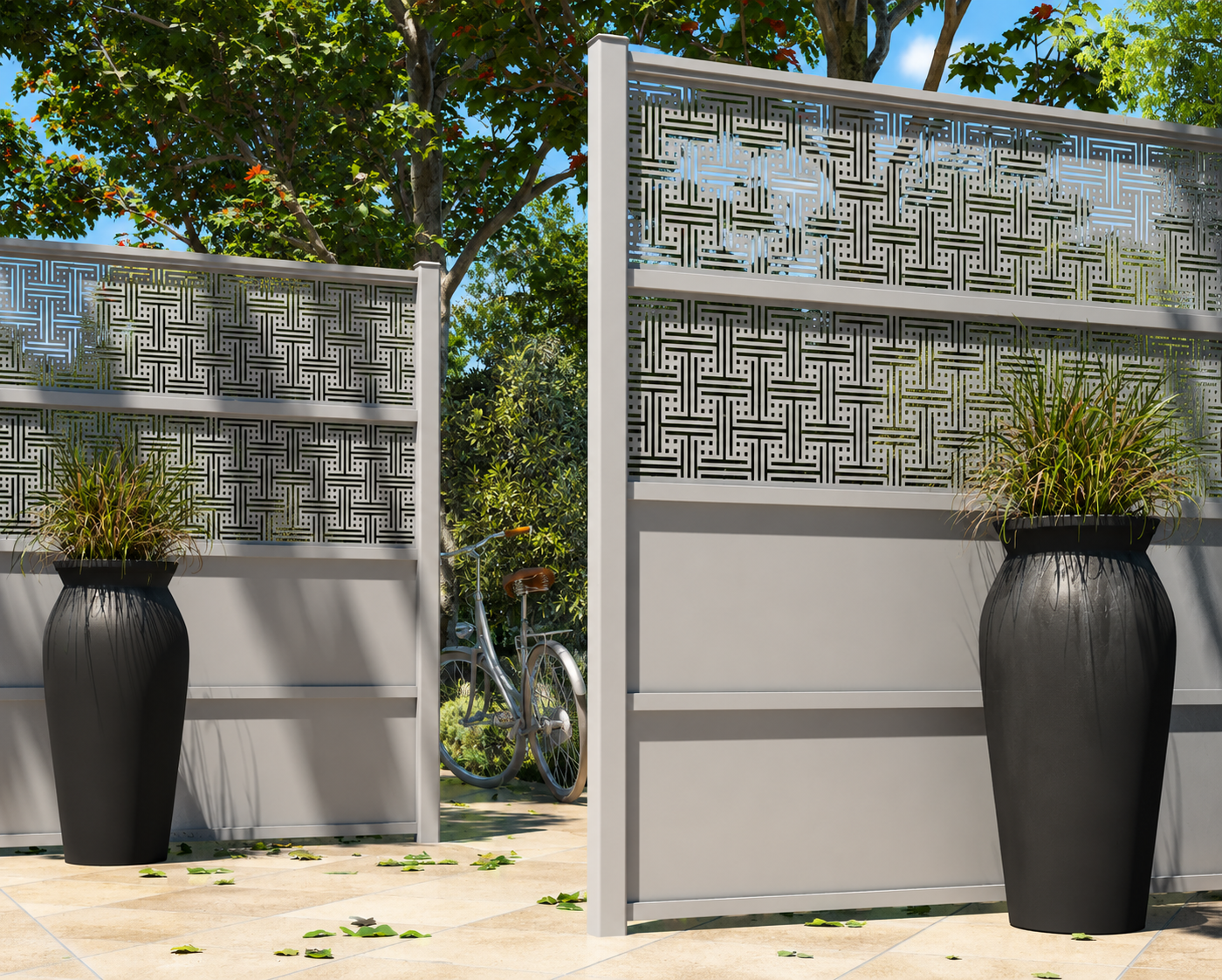 Portail d'entrée extérieur en métal gris avec motifs géométriques, flanqué de grands pots noirs contenant des plantes hautes, sol carrelé clair avec feuilles tombées, et vélo blanc visible en arrière-plan dans un jardin verdoyant.
