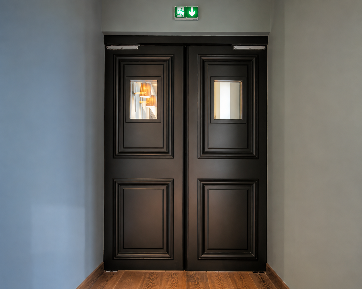 Porte double noire élégante avec petites fenêtres carrées, au-dessus une signalisation de sortie de secours lumineuse verte avec flèche vers le bas.