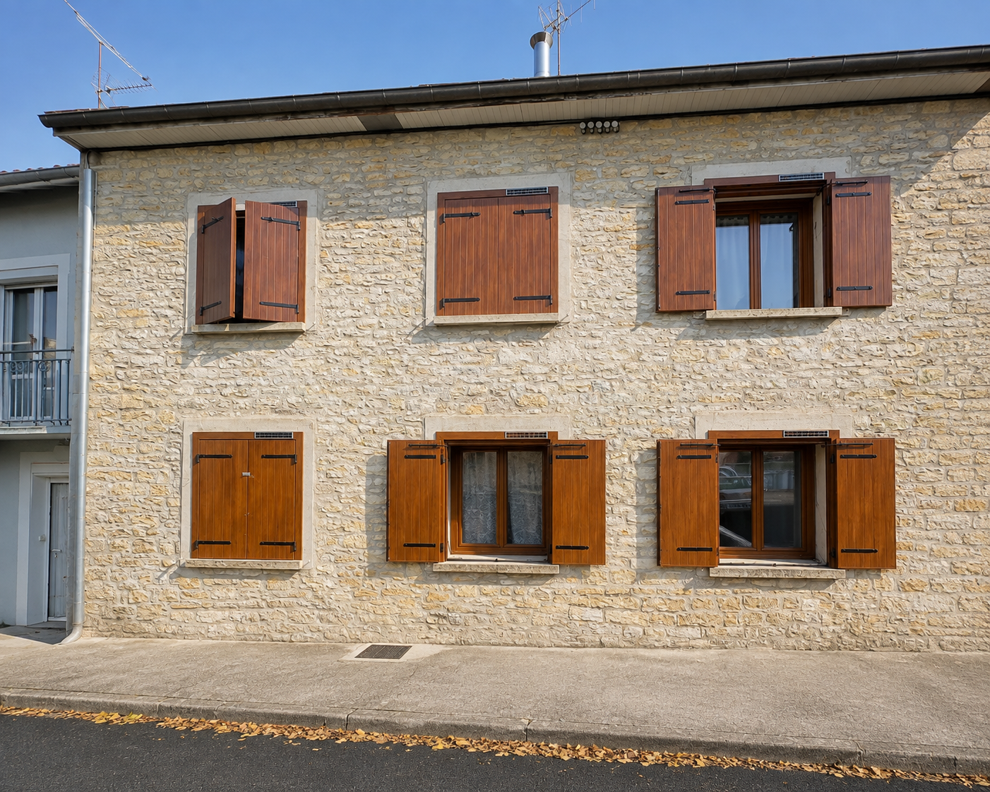 Façade en pierre avec six fenêtres décorées de volets en bois marron, certains ouverts et d'autres fermés, sous un ciel bleu clair.