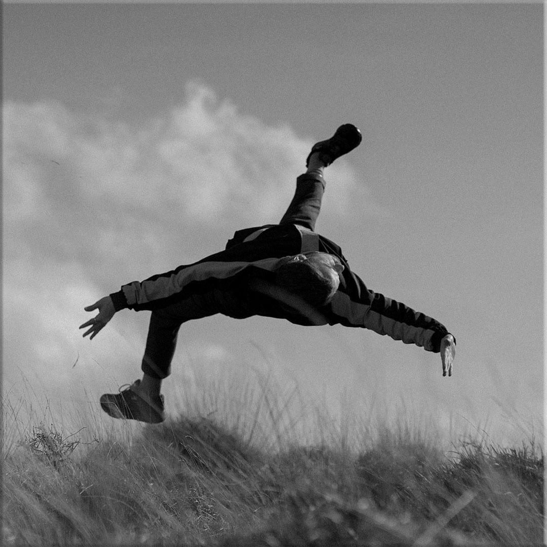 Person performing an acrobatic jump or flip outdoors above grass with arms spread wide.