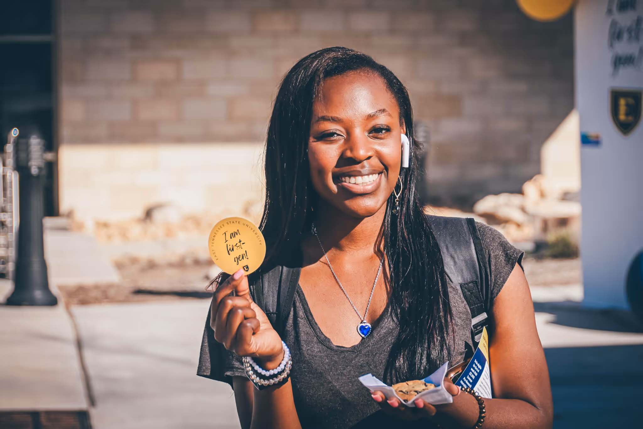 Student smiling while holidng a sticker that says "I am first-gen!"