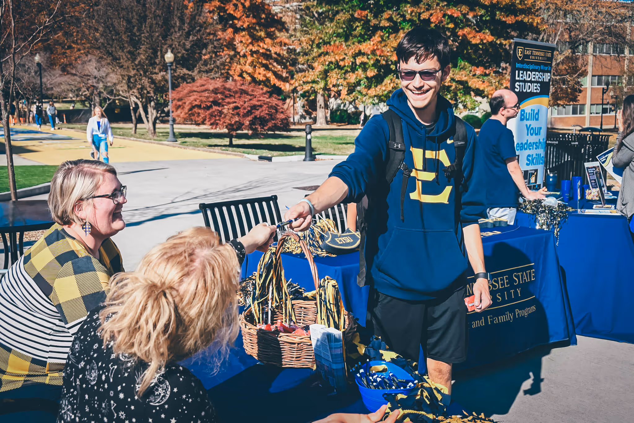 Student standing at a table talking to two staff members