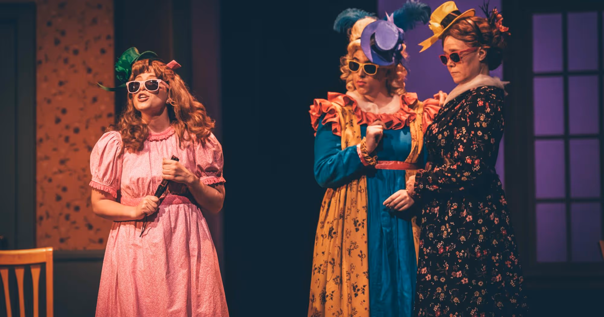 3 actors in long dresses, hats and sunglasses performing