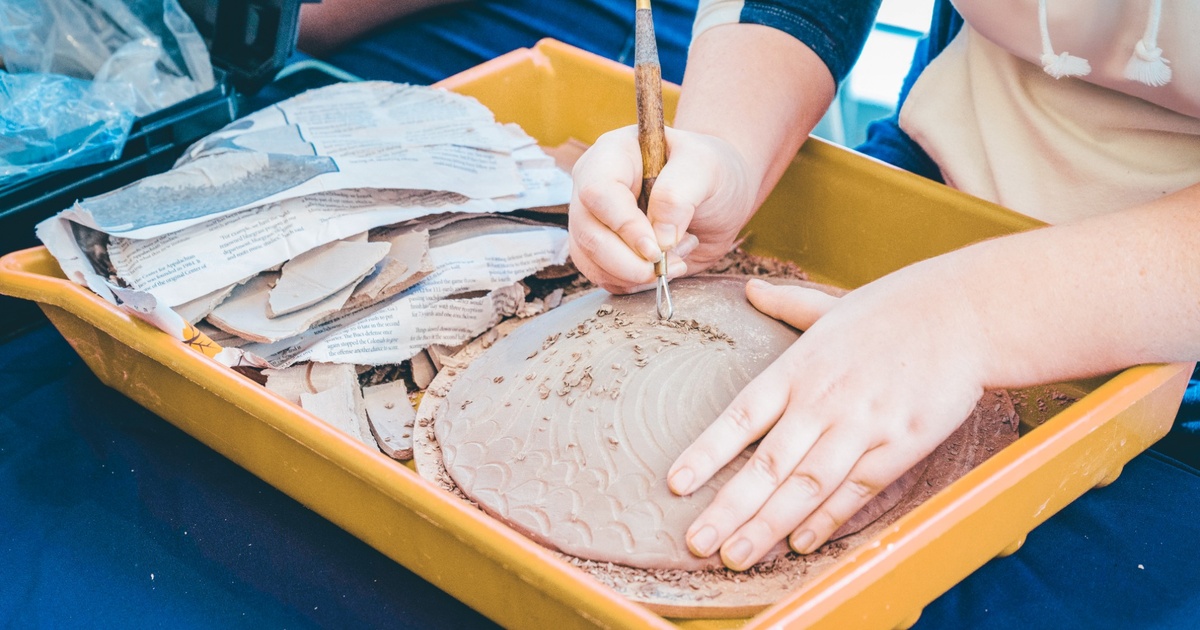 An ETSU student carves a detailed design into a clay project during an art class.