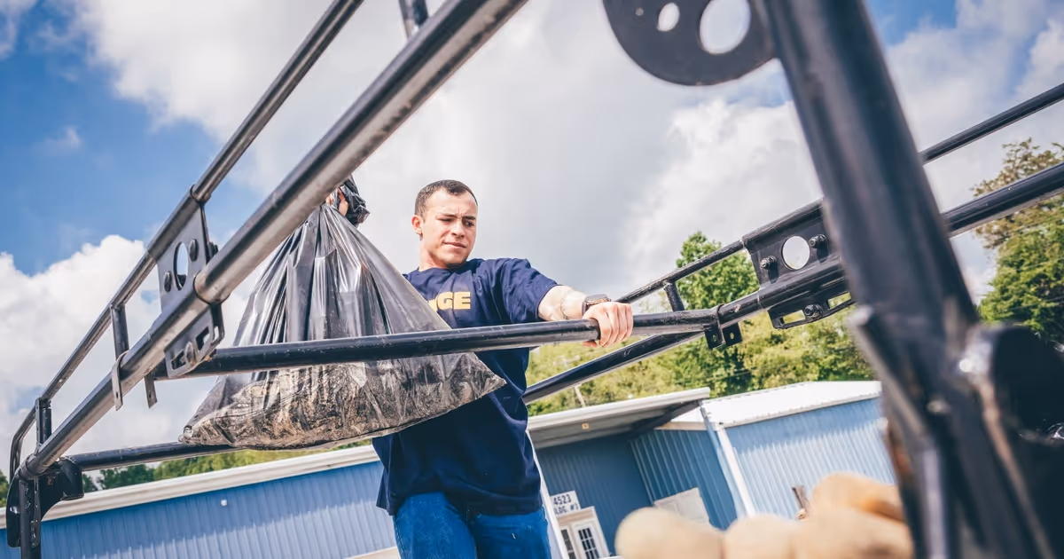 Person tossing debris into a large blue dumpster outside.