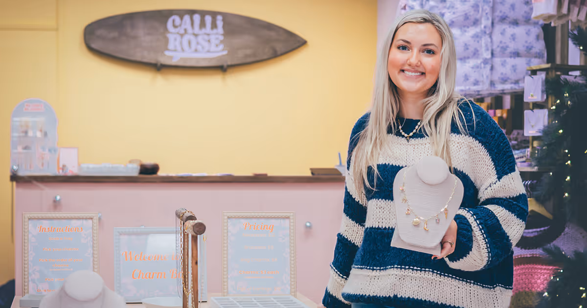 ETSU alum Callie Hall poses in her shop, Calli Rose, with several jewelry stands around her.