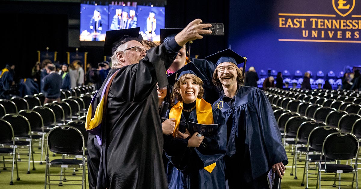Graduates in caps and gowns take a selfie together on the floor of an ETSU commencement ceremony.