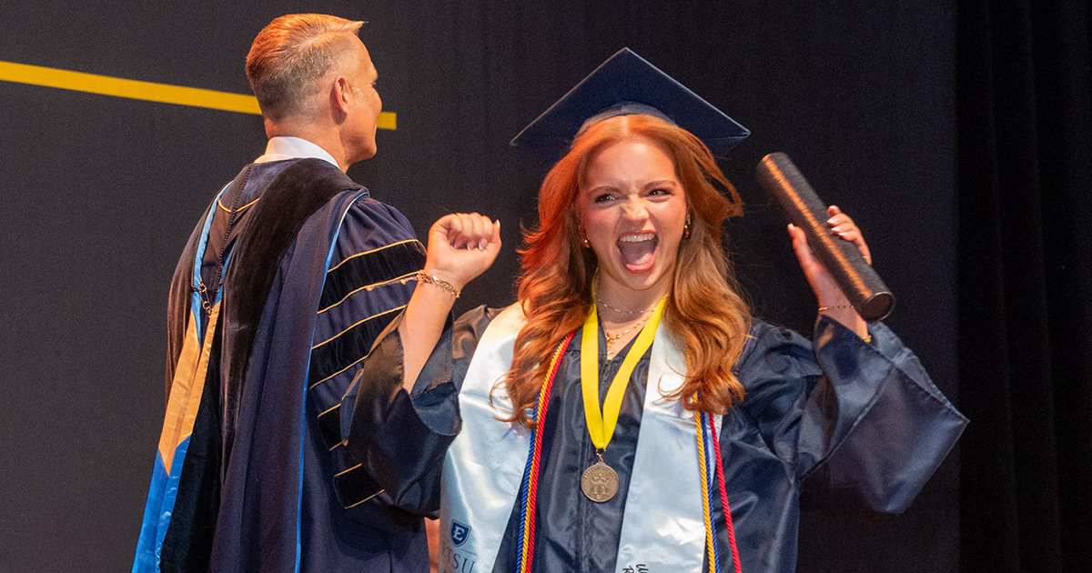 A student cheers as she crosses the stage to collect her diploma