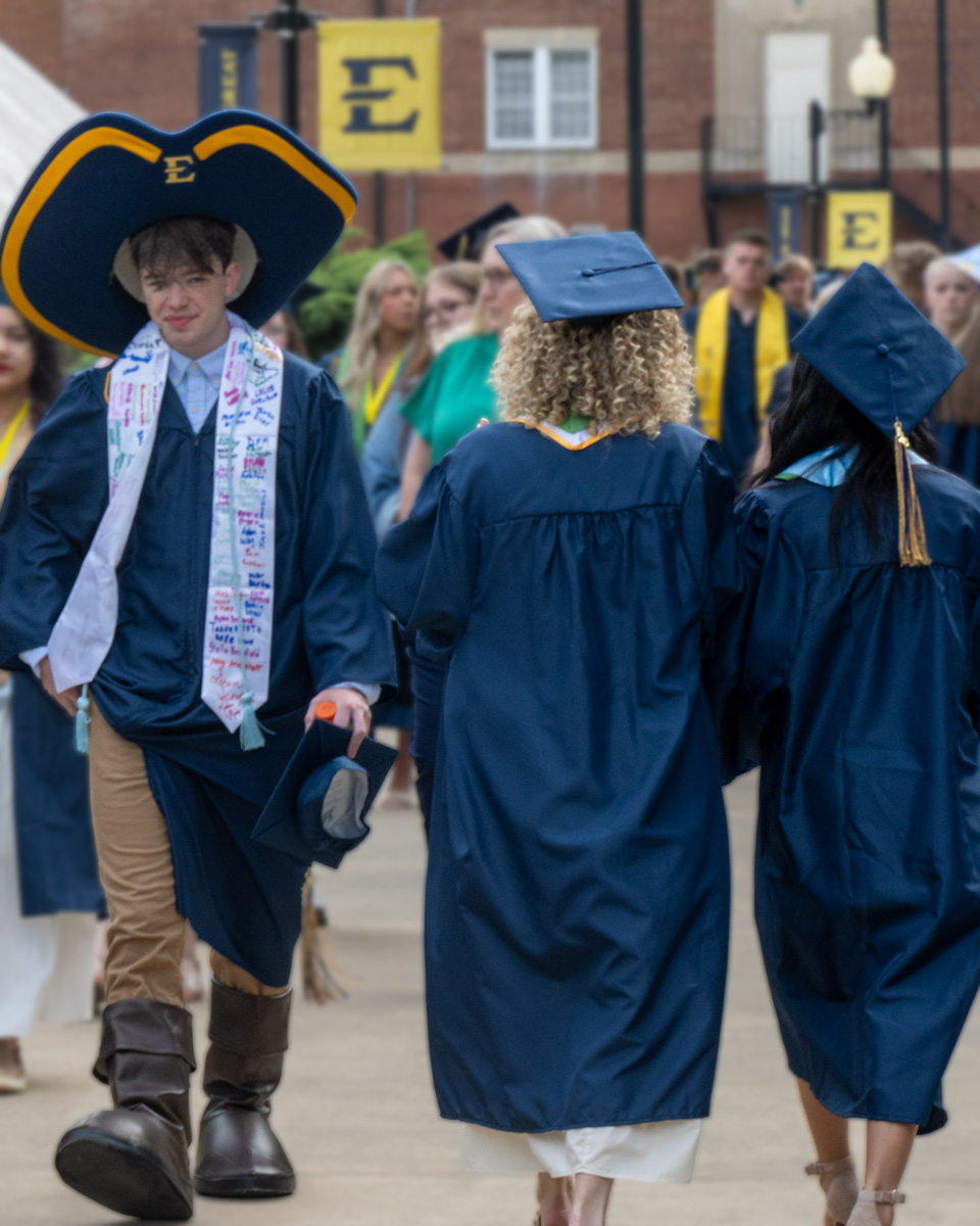 Bryce Ward walks toward graduation wearing Bucky, the mascot's, hat