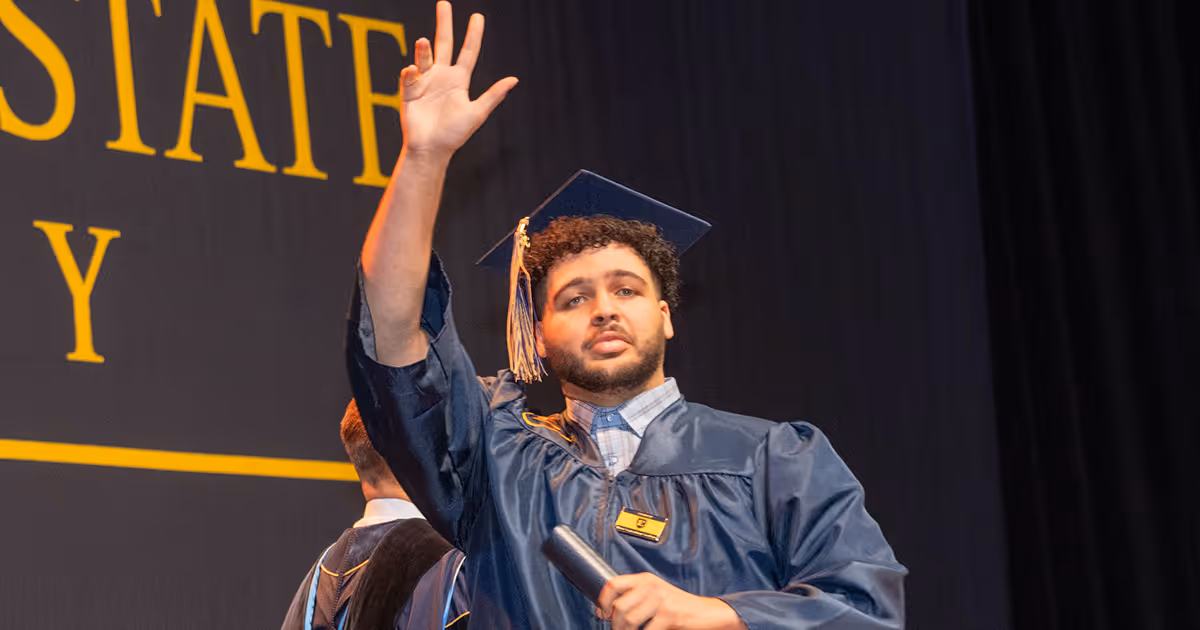 A student raises his hand to wave as he crosses the graduation stage