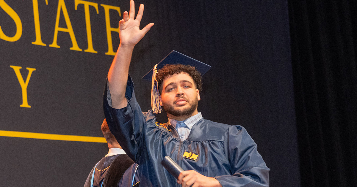 A student raises his hand to wave as he crosses the graduation stage
