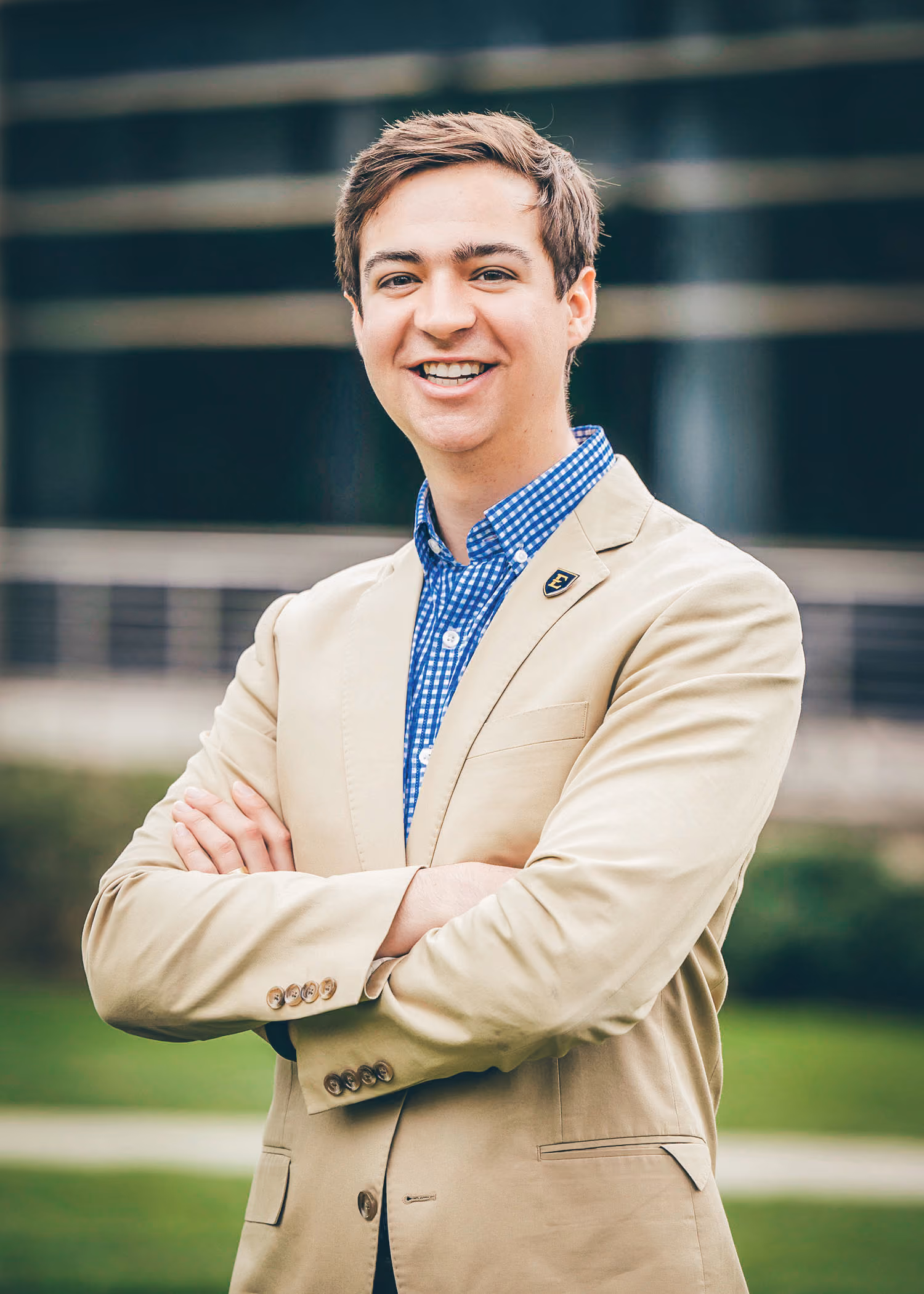 A photo of Timothy Lewis outside. He is wearing a tan suit and has his arms crossed over his chest as he smiles.