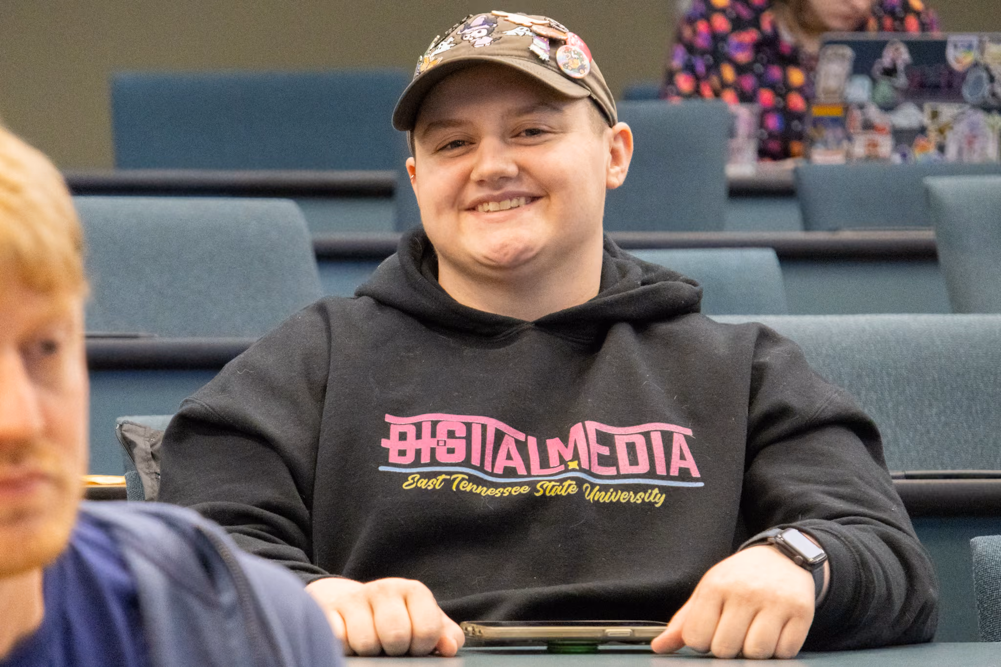 A person smiles as they wear an ETSU digital media hoodie.