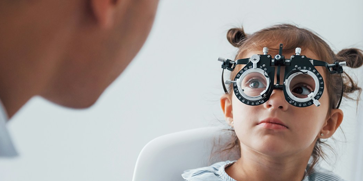 A child wearing a trial frame during a vision therapy exam, with the doctor looking on.