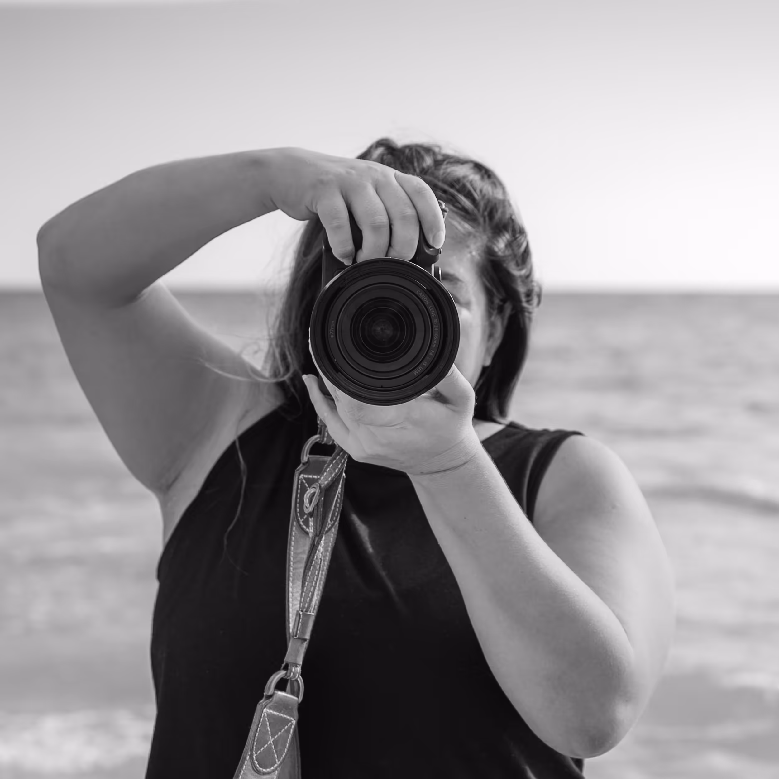 Person holding a camera and taking a photo at the beach.