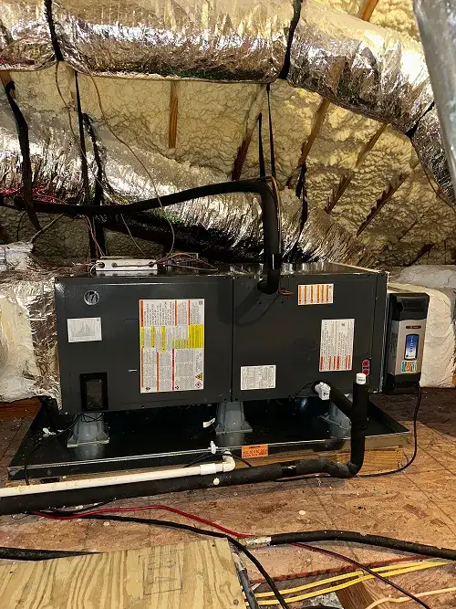 Industrial HVAC unit installed in an attic with insulated ductwork and wooden floor.