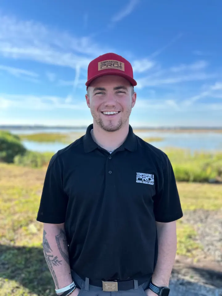 Smiling man outdoors wearing a red Temperature Pro cap and black polo shirt with a lake and blue sky in the background.