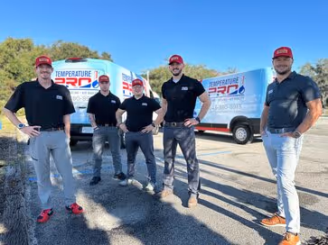 Five men wearing red caps and black shirts posing outdoors on a sunny day in front of two white vans with Temperature Pro logos.