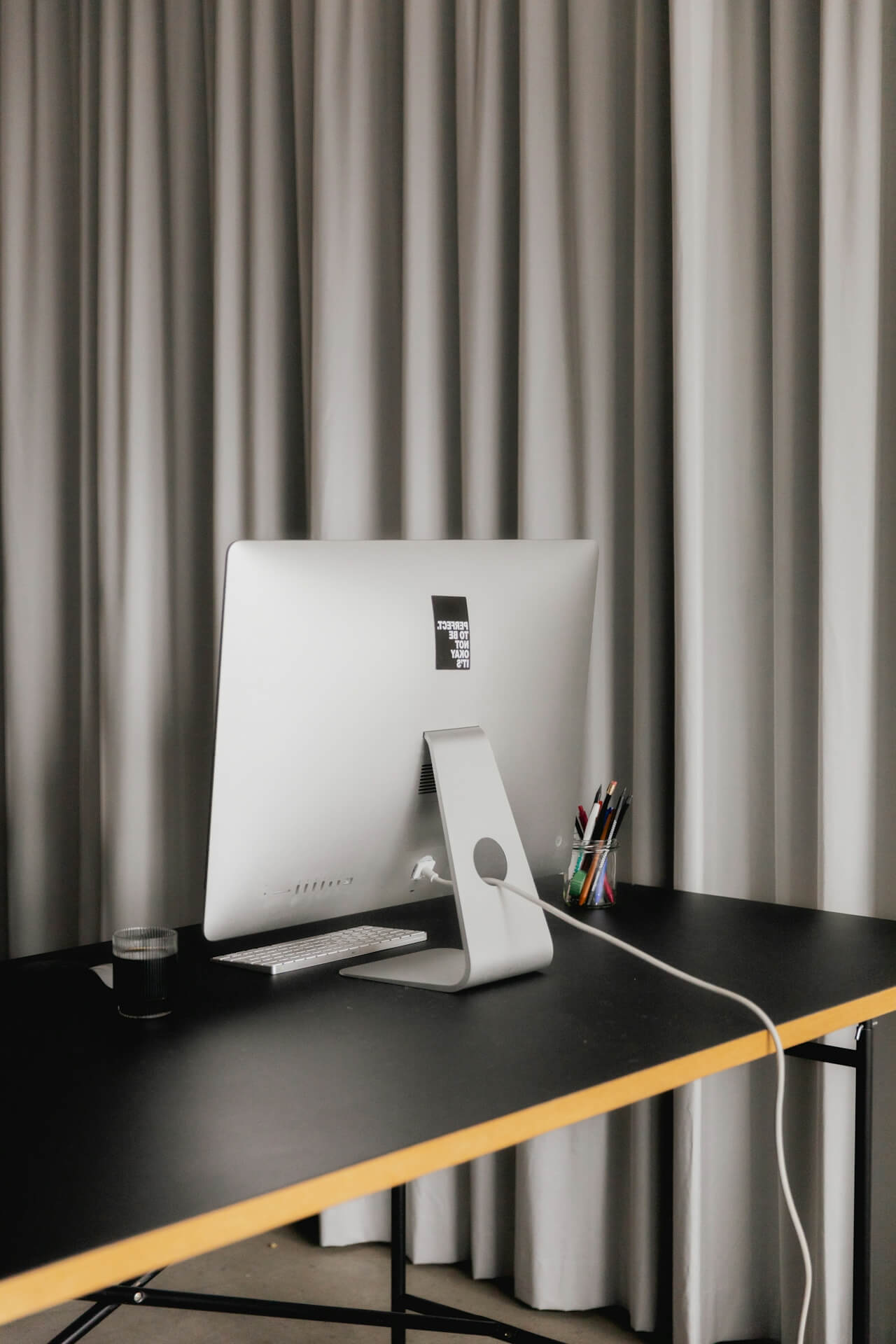 Desktop computer on a black desk in front of grey curtains